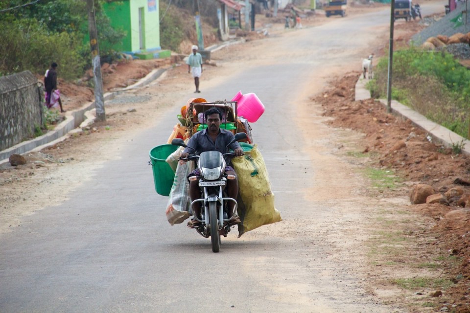 Man riding motorcycle with a large amount of stuff hanging off of it